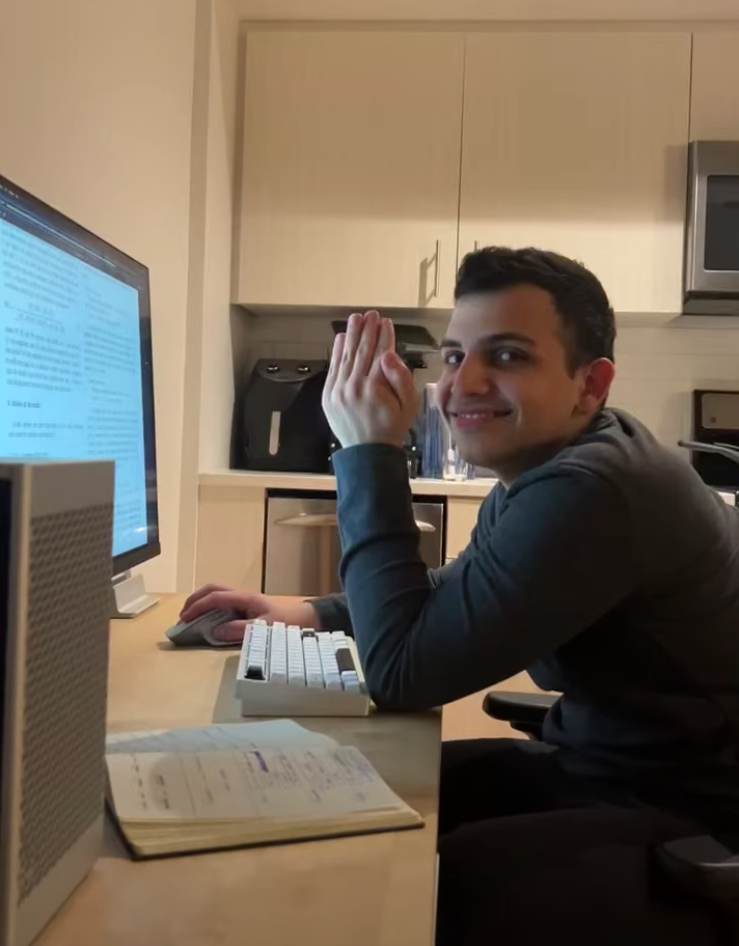 Amirali sitting at his desk with a monitor and notebook at home